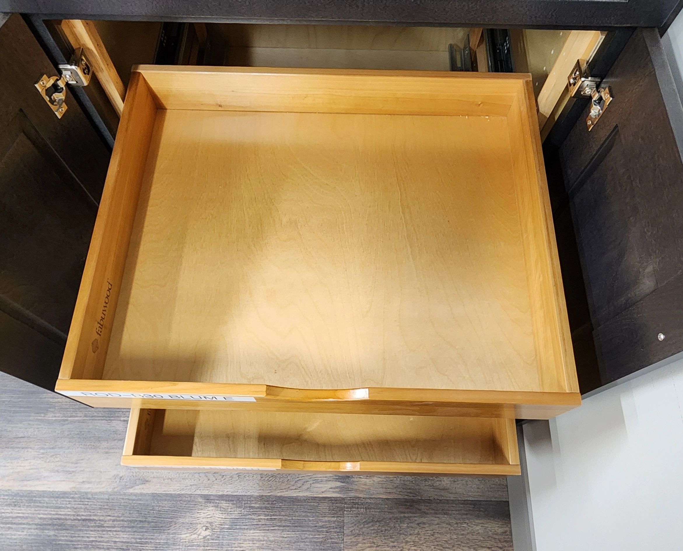 Open wooden drawers inside a dark cabinet on a wooden floor.