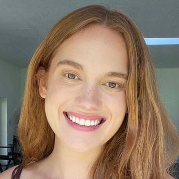 Smiling young woman with red hair and green eyes in natural light.