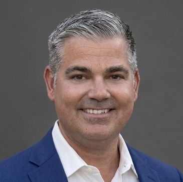 Smiling man in a blue suit with gray hair against a gray background.