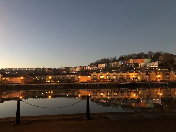 Bristol skyline at dusk. There are lights and colourful houses across the river.