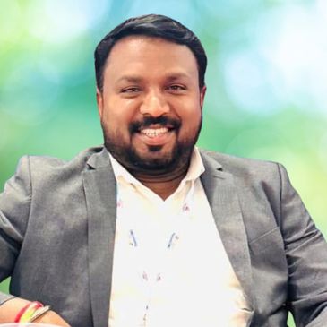 Smiling man in a suit with a conference badge, seated casually.
