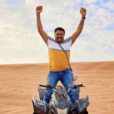 Man joyfully posing on an ATV in the desert with hands raised.