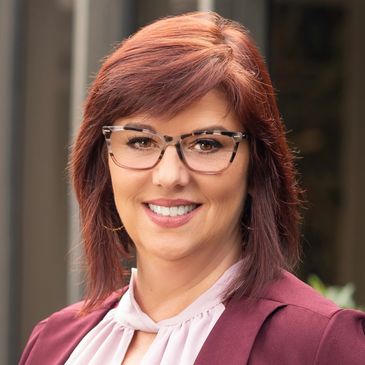 Smiling woman with glasses and red hair in professional attire.