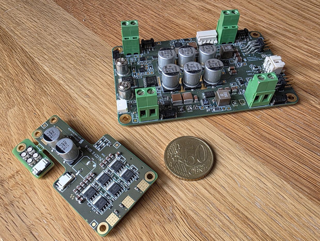 Two electronic circuit boards and a 50 cent euro coin on a wooden surface.
