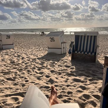 Beach scene with striped beach chairs, sand, and a book in the foreground.