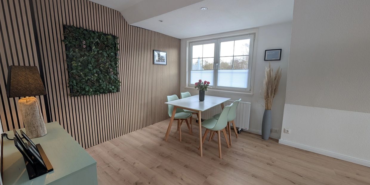 Minimalist dining area with a white table, green chairs, and a plant wall feature.