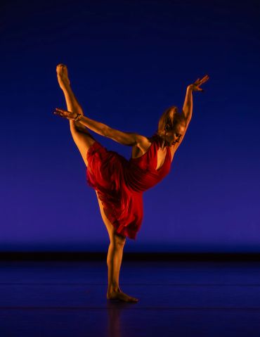 A dancer in a red dress gracefully poses on stage against a blue backdrop.