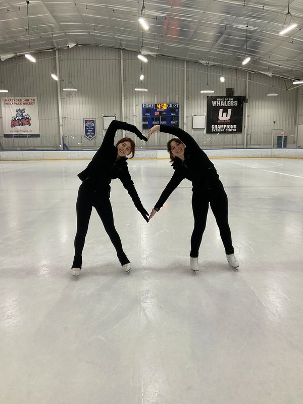 Two ice skaters forming a heart shape with their arms on the rink.