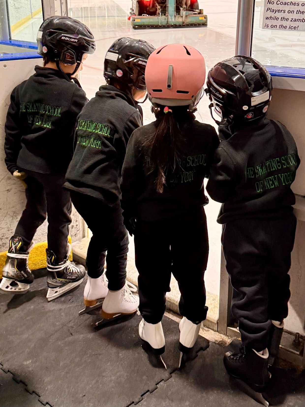 Four children in helmets and black jackets from The Skating School of New York.