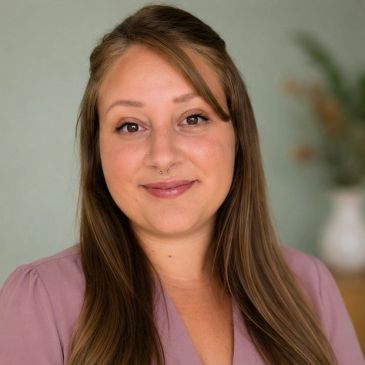 Smiling woman with long hair and a septum piercing.