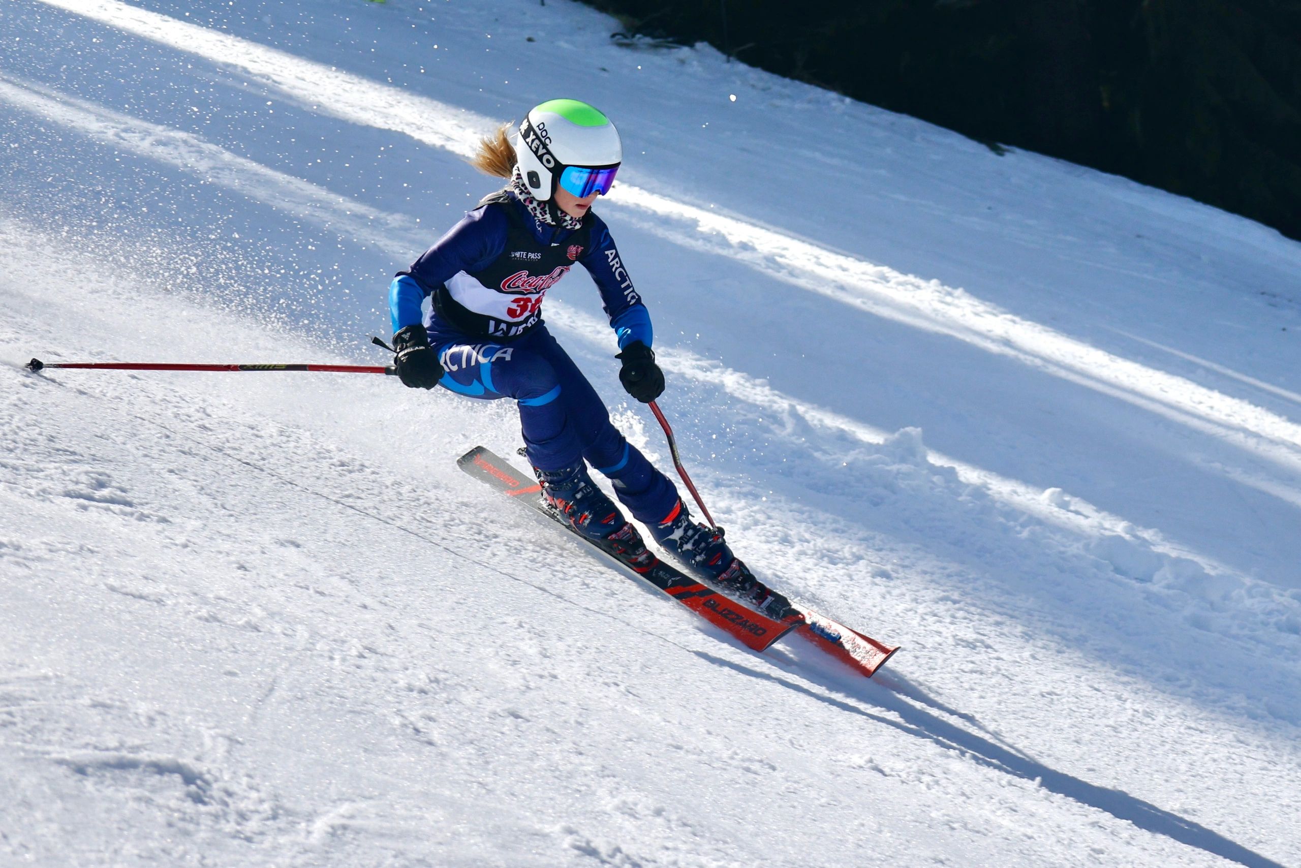 Ski racer in blue racing downhill on snowy slope with helmet and goggles, red skis and poles