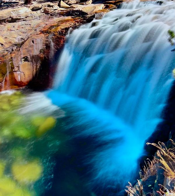 long exposure of a waterfall emptying into a green looking pool under reddish rocks
