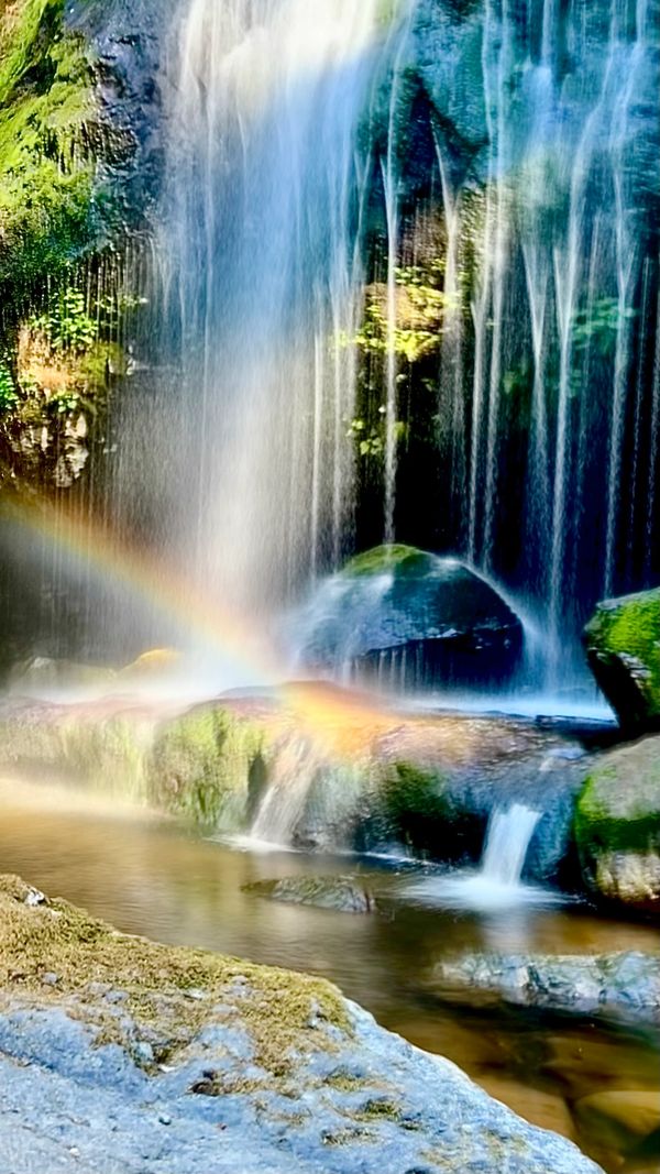 rainbow in front of a long exposure of a beautiful waterfall and mossy rocks