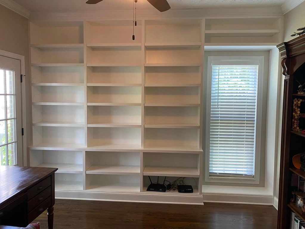 Empty white built-in bookshelves next to a window with blinds.