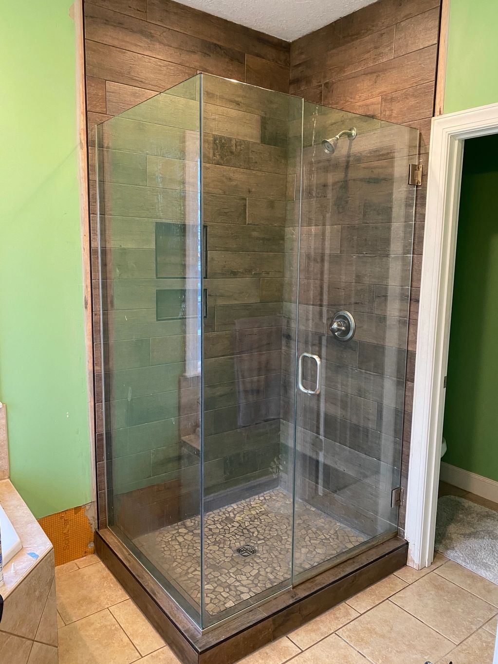 Glass shower with wooden tile walls and pebble floor.