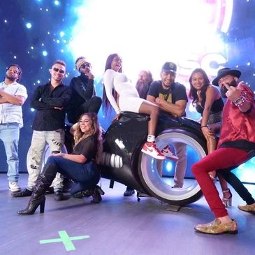 Group of people in front of a virtual backdrop on and surrounding a stationary motorcycle 