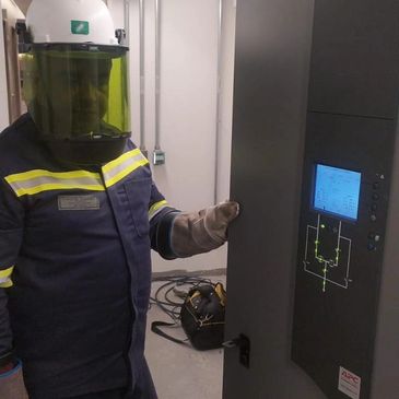 Worker in protective gear operating electrical control panel.
