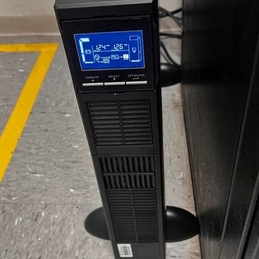 A black UPS device with a blue digital display showing voltage readings.