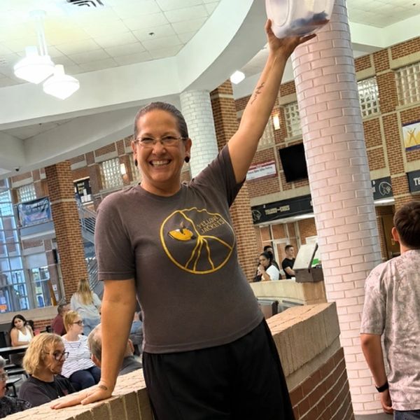 Smiling woman in a school hallway holding a container.