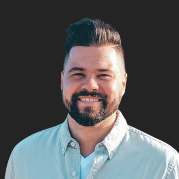 Smiling man with beard and dark hair in light shirt.