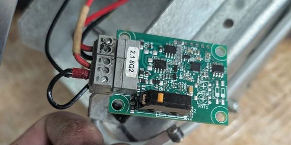 Hand holding a small circuit board with wires.