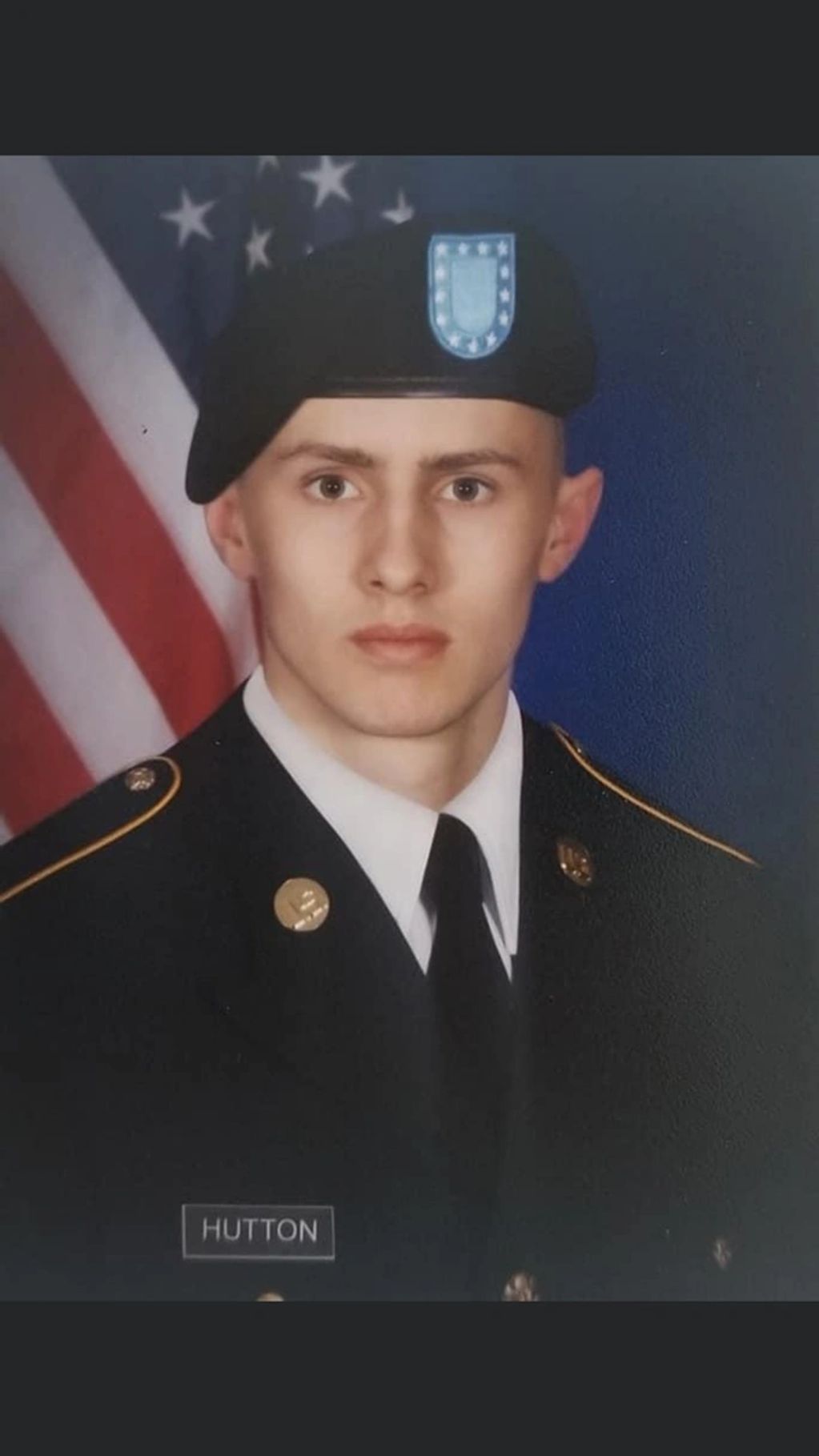 Young soldier in formal military uniform with an American flag backdrop.