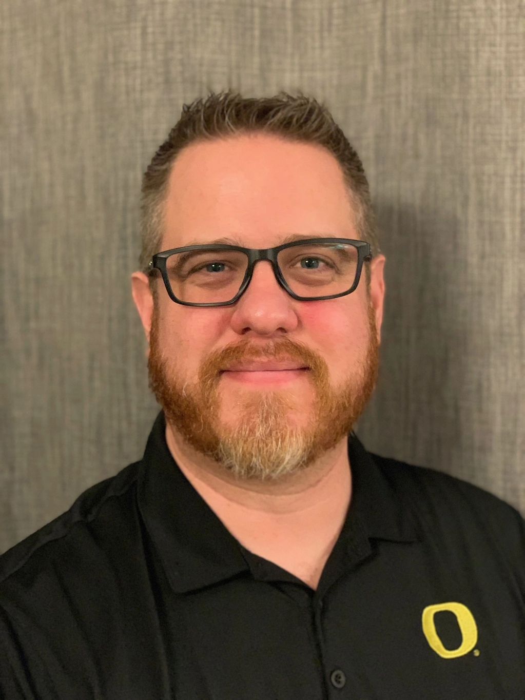 Man with glasses and beard wearing a black shirt with a yellow 'O' logo.