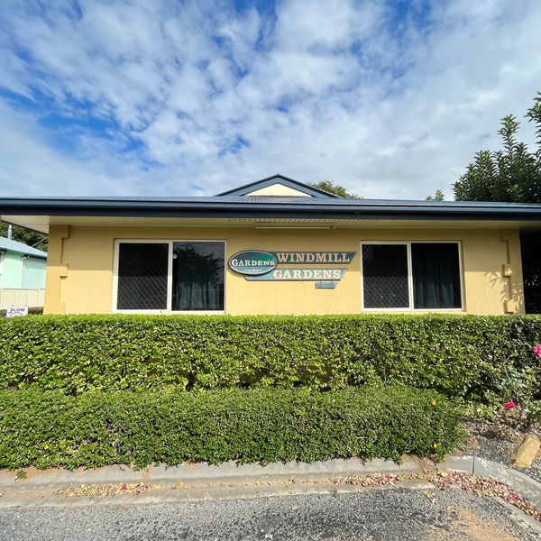 Yellow building with a sign reading Windmill Gardens and green hedges in front.