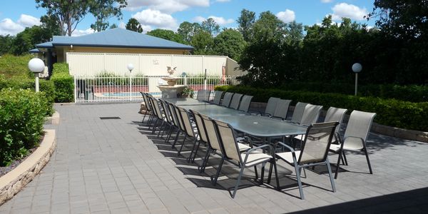 Outdoor patio with a long dining table and chairs under a sunny sky.