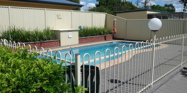 A fenced backyard swimming pool with greenery and a clear blue sky.