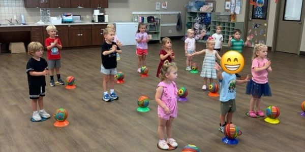 Young children in a gym class practicing with basketballs.