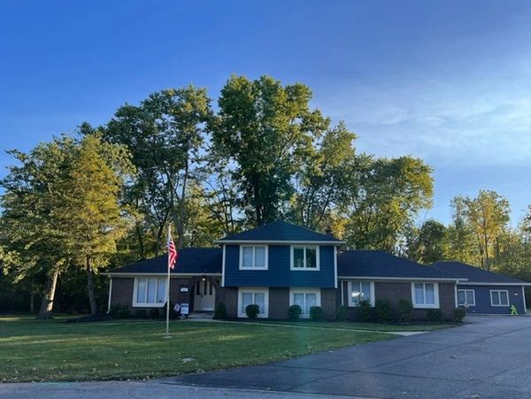 A suburban house with brick facade and blue siding under a clear sky.