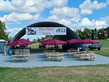 Outdoor picnic area with tables and purple umbrellas under a large arch.