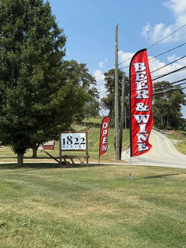 Red flags advertising beer, wine, and open winery by a country road.