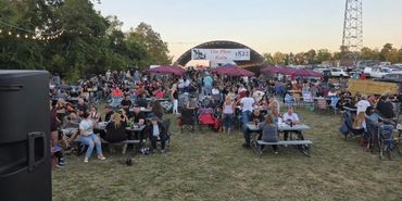 Crowd gathered outdoors for an event at dusk with seating and umbrellas.