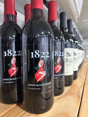 Bottles of 1822 Sweet Black Cherry wine lined up on a wooden shelf.