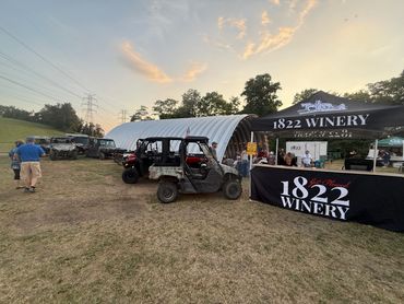 Outdoor winery event with utility vehicles and a tent at sunset.