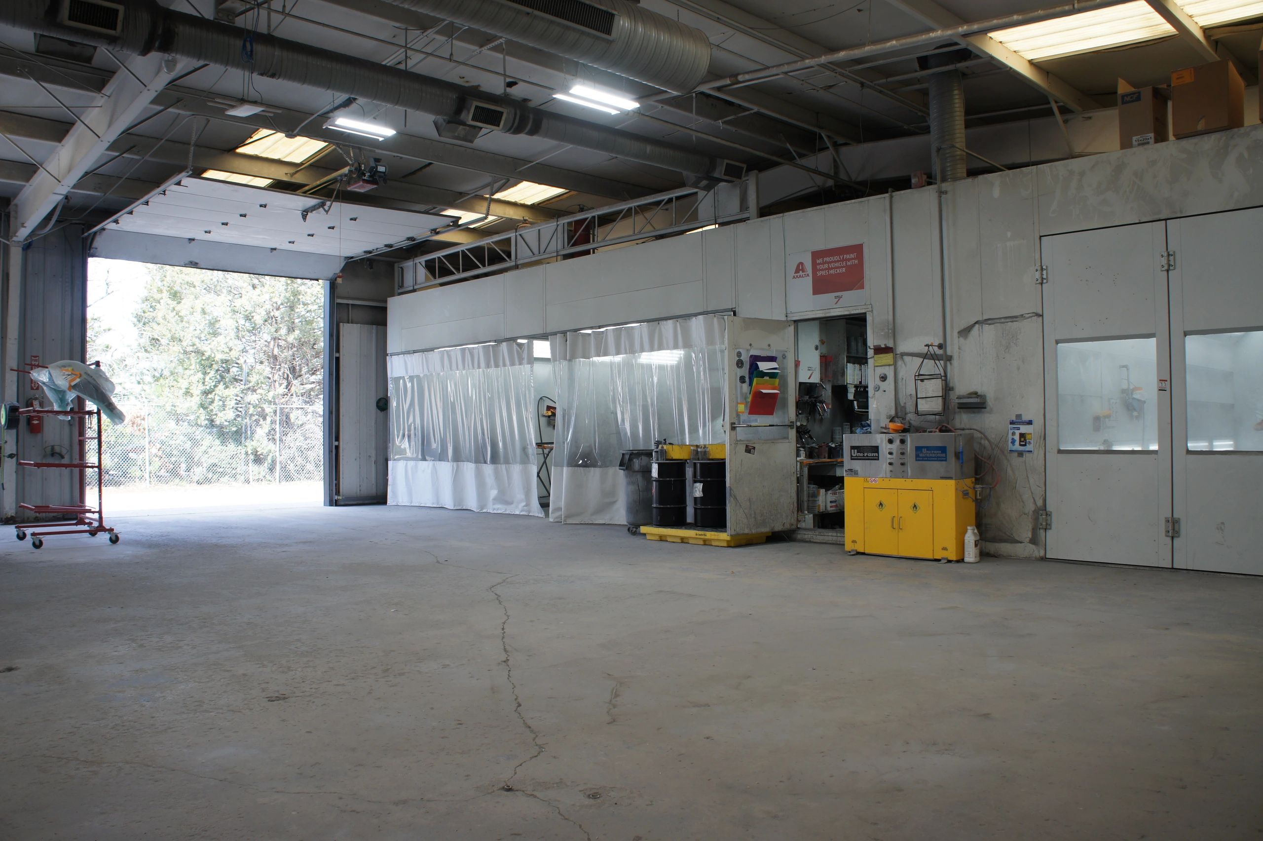 Interior of a spacious industrial workshop with open garage door and equipment.