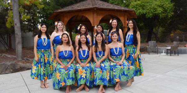 Group of women in colorful traditional Hawaiian dresses posing outdoors.