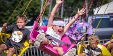 Children joyfully swinging on a colorful swing ride at an outdoor fair.