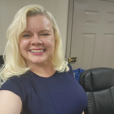 Smiling woman with blonde hair wearing a navy blue top in an office setting.