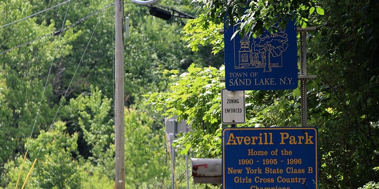 Signage marking the town of Sand Lake, NY, and Averill Park with lush greenery around.