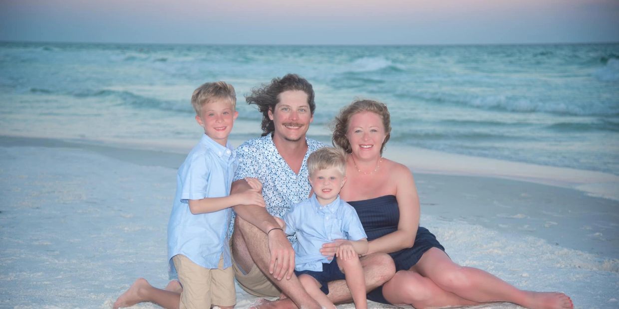 A happy family of four sitting on the beach at sunset.