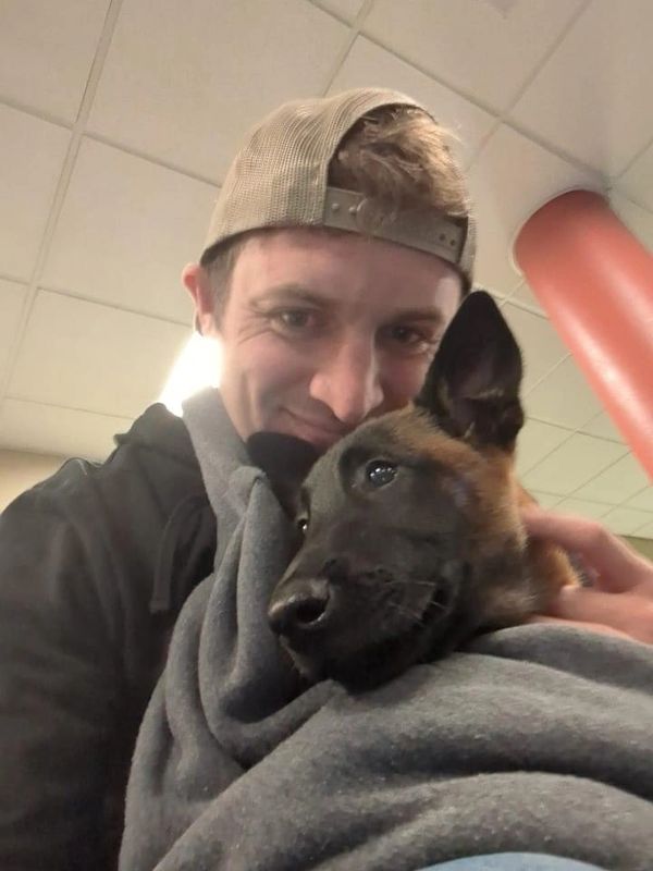 Man in cap cuddling a calm dog indoors.