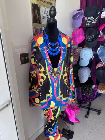 Colorful patterned suit on a mannequin with blue beaded necklace and pink boots.