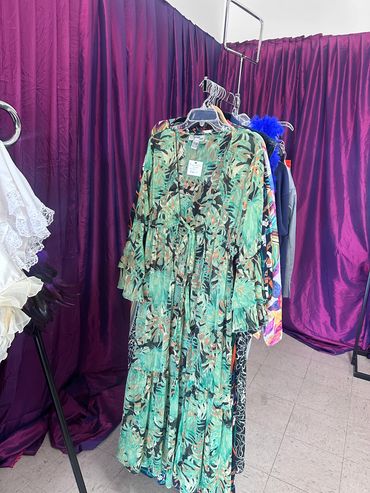 Green floral maxi dress hanging on a rack with purple curtains in the background.