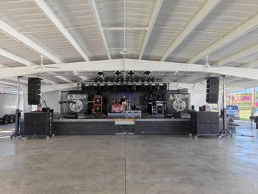 Empty stage set up for a live music performance under a covered pavilion.