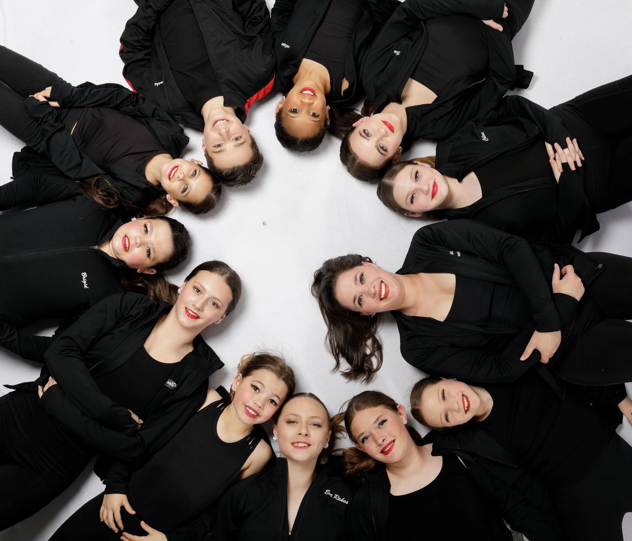 Group of young women in black outfits lying in a circle, smiling at the camera.