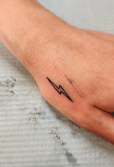 Tiny lightning bolt tattoo on hand.