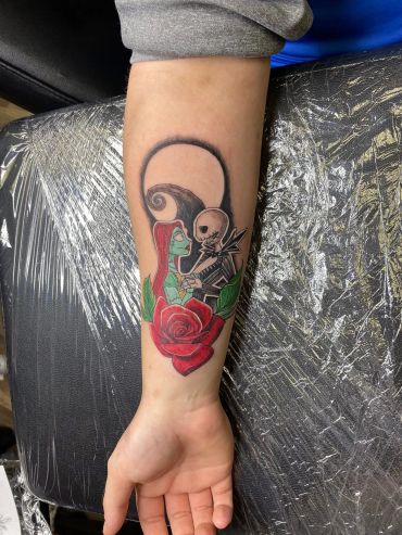Tattoo of characters with a red rose on forearm.